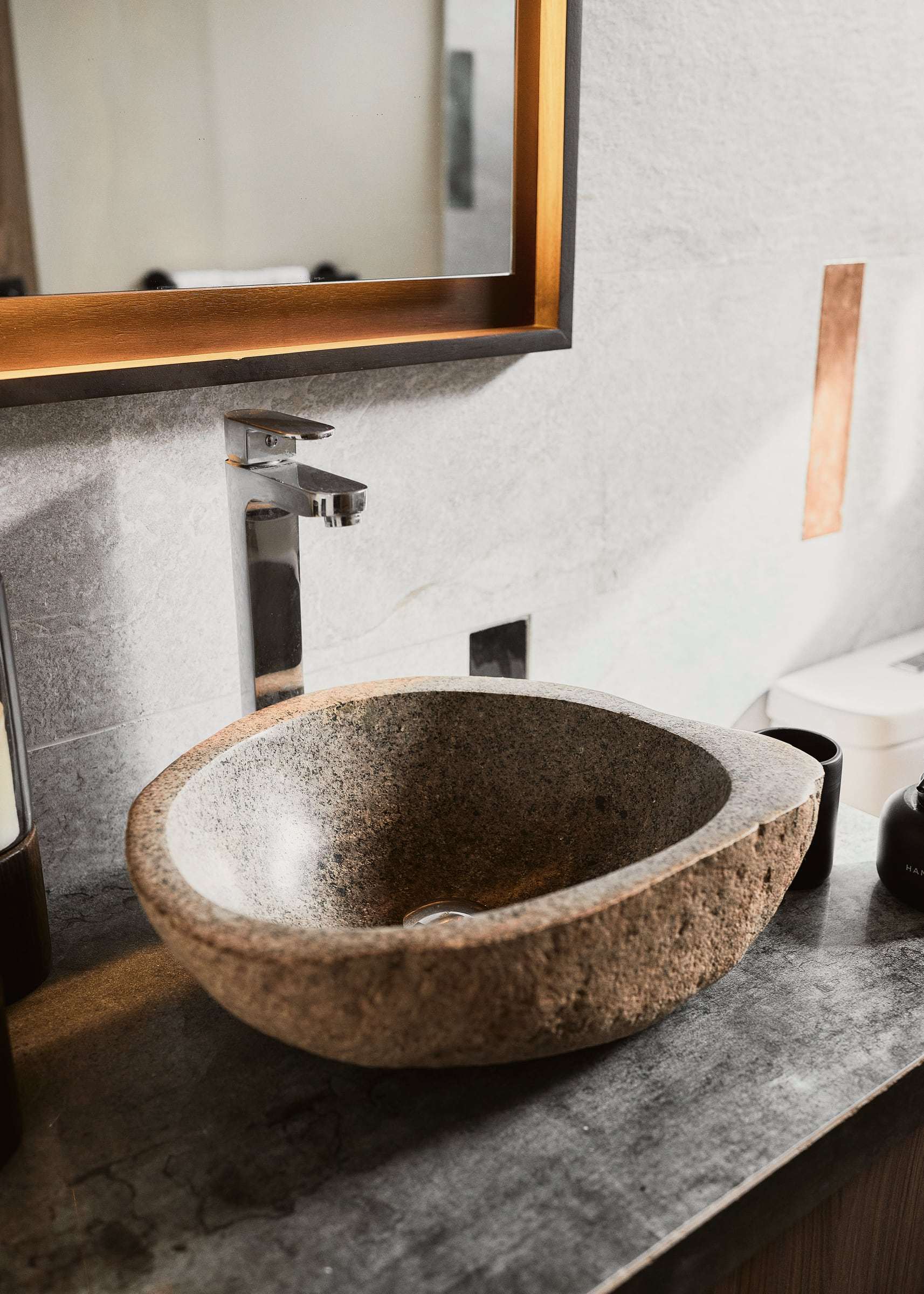 River-stone vessel sink on a dark stone counter in a Conga guest bathroom