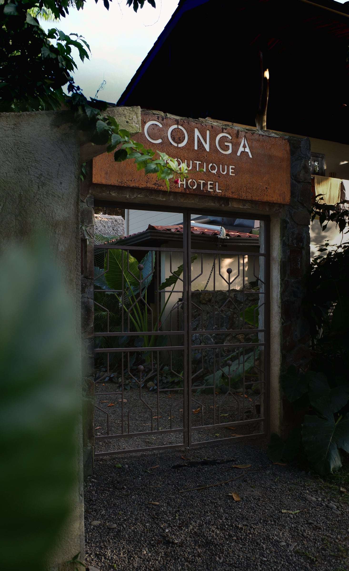 Street gate beneath the rusted-steel Conga Boutique Hotel sign, the garden glimpsed through the bars