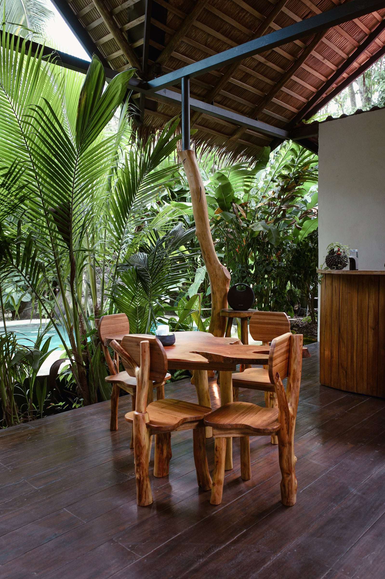 Hand-carved wooden table and chairs on the rancho deck, the pool glimpsed through the palms