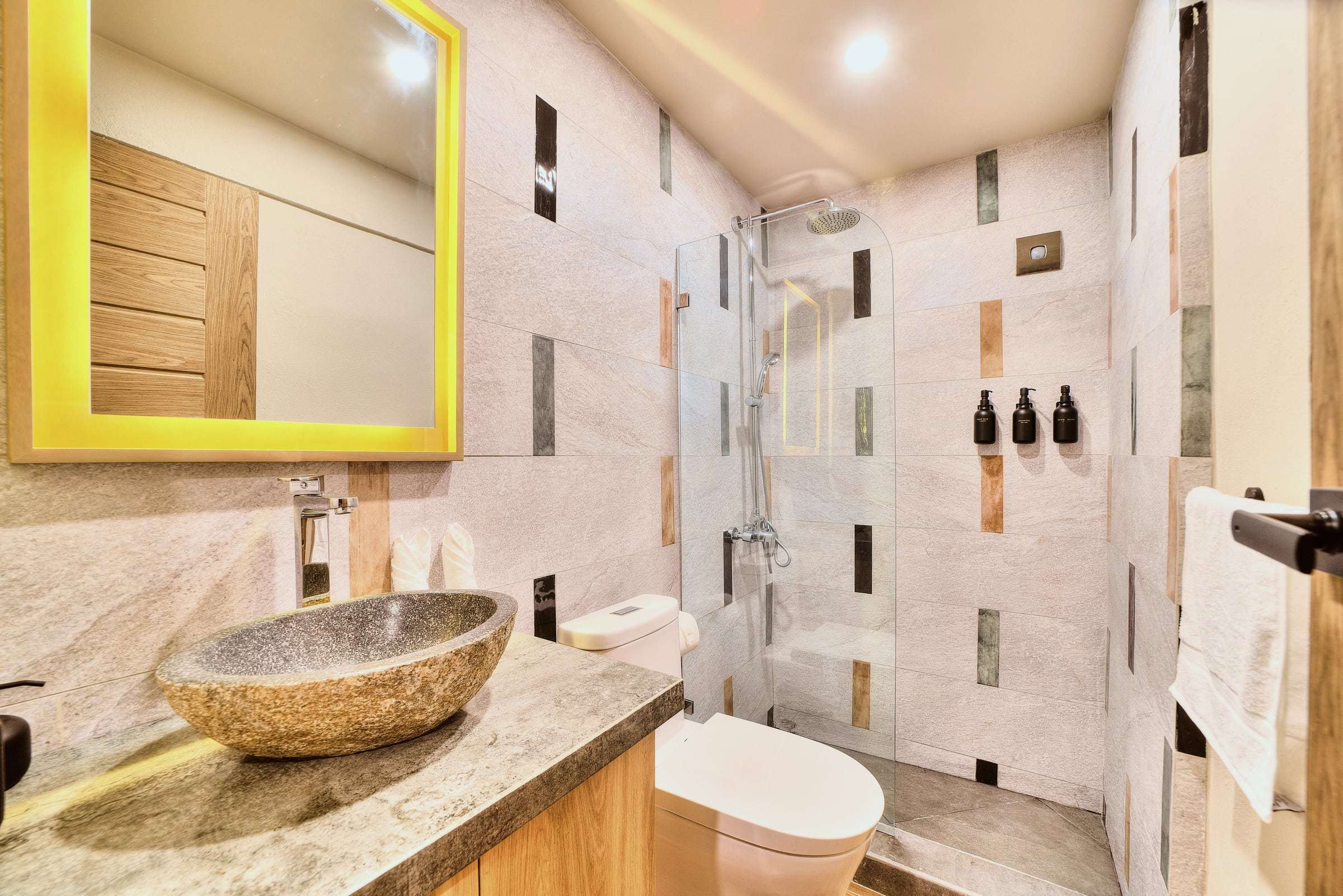 Deluxe Garden King bathroom: river-stone vessel sink, yellow-lit mirror and a walk-in rain shower with glass screen