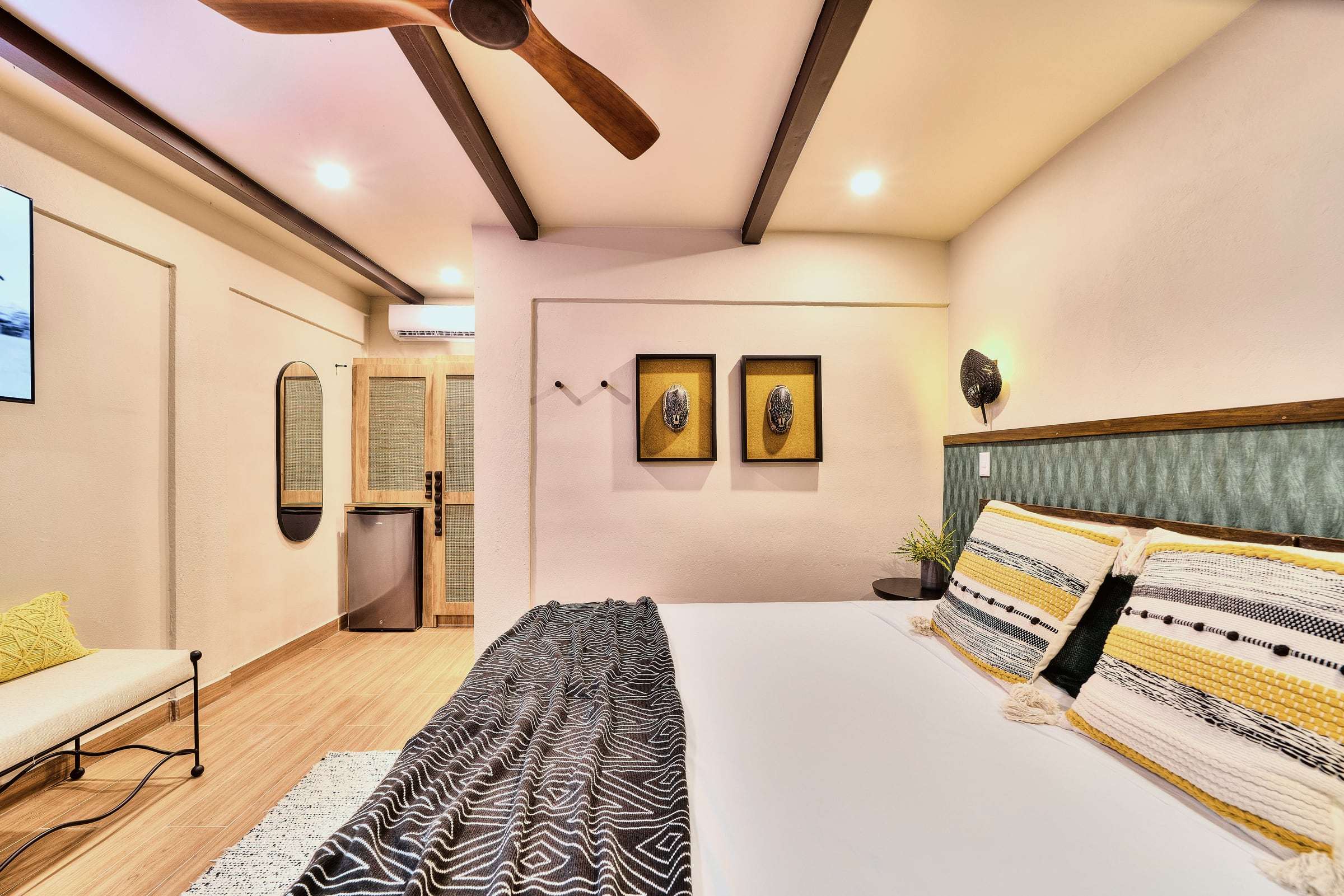 Deluxe Garden King: king bed with striped cushions, green headboard wall, framed masks, an oval mirror and a bench