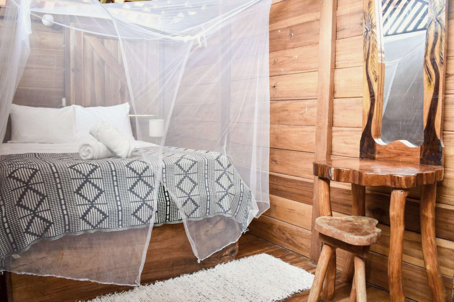 Garden Home second bedroom: netted bed with a geometric throw, carved-wood vanity with mirror and a stool