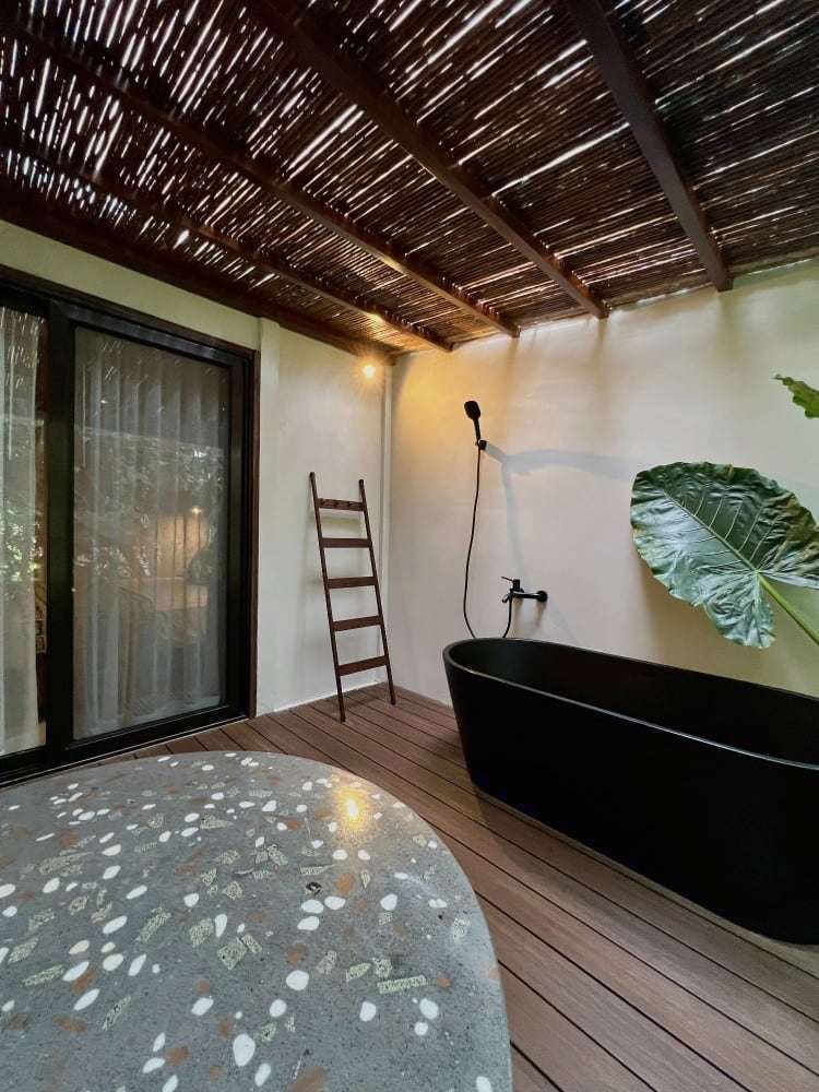 Grand Oasis Suite open-air bath deck: black soaking tub, ladder towel rack and sliding doors under a cane pergola