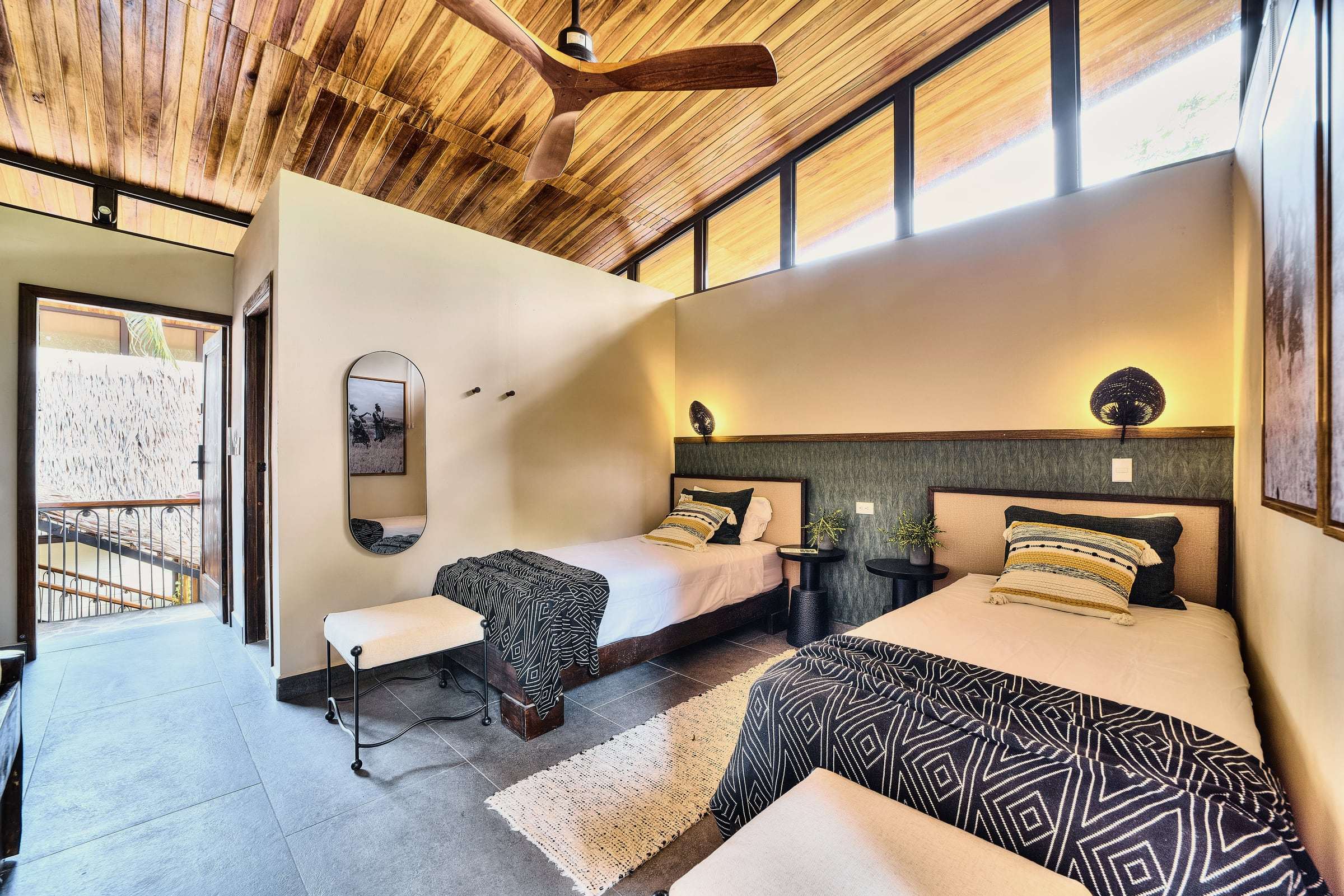 Jungle View Suite with twin beds under clerestory windows and a sloping wood ceiling, door open to the balcony