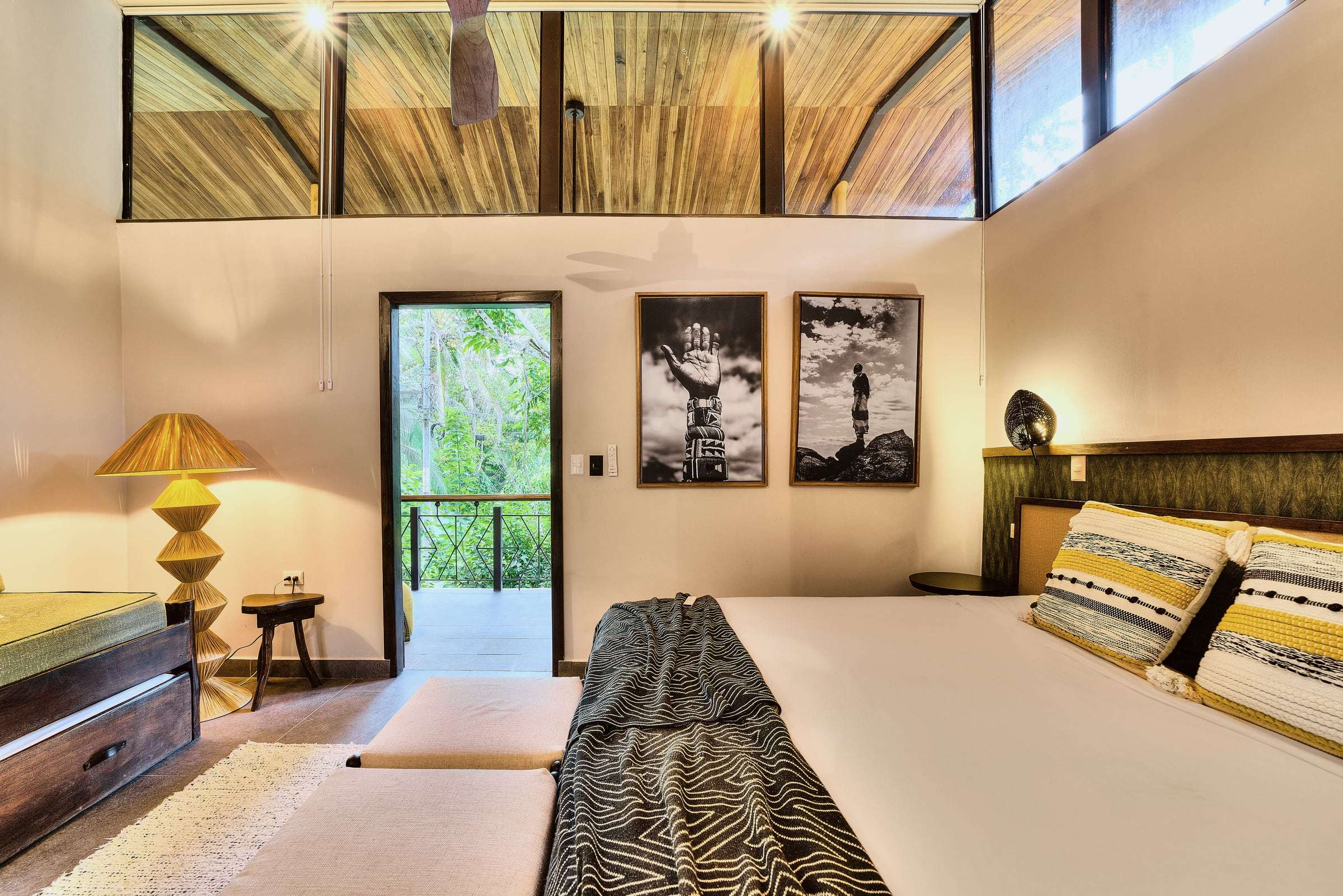 Jungle View Suite: king bed with striped cushions, raffia lamp, two black-and-white prints and a door open to the jungle