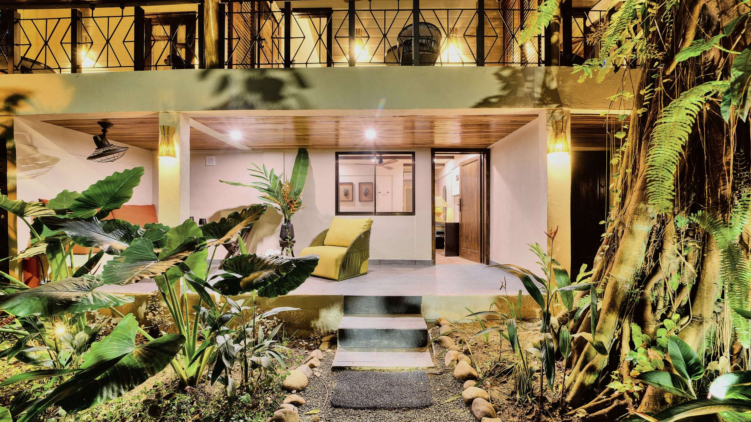 Superior Garden Room terrace at night: yellow armchair on a lit porch, steps up from the garden path, balcony above