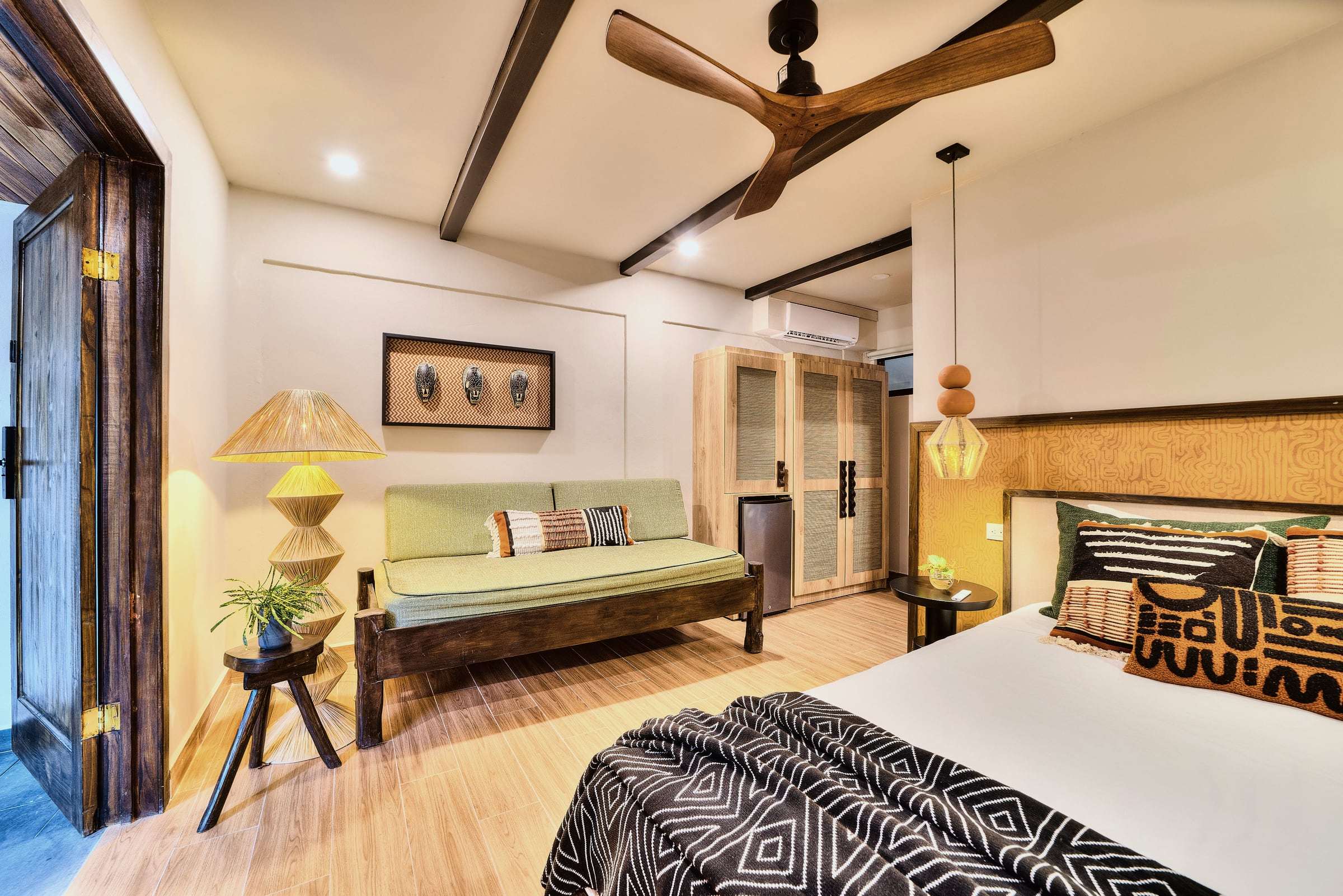 Superior Garden Room: bed, green daybed, raffia floor lamp, framed masks and dark ceiling beams with a wooden fan
