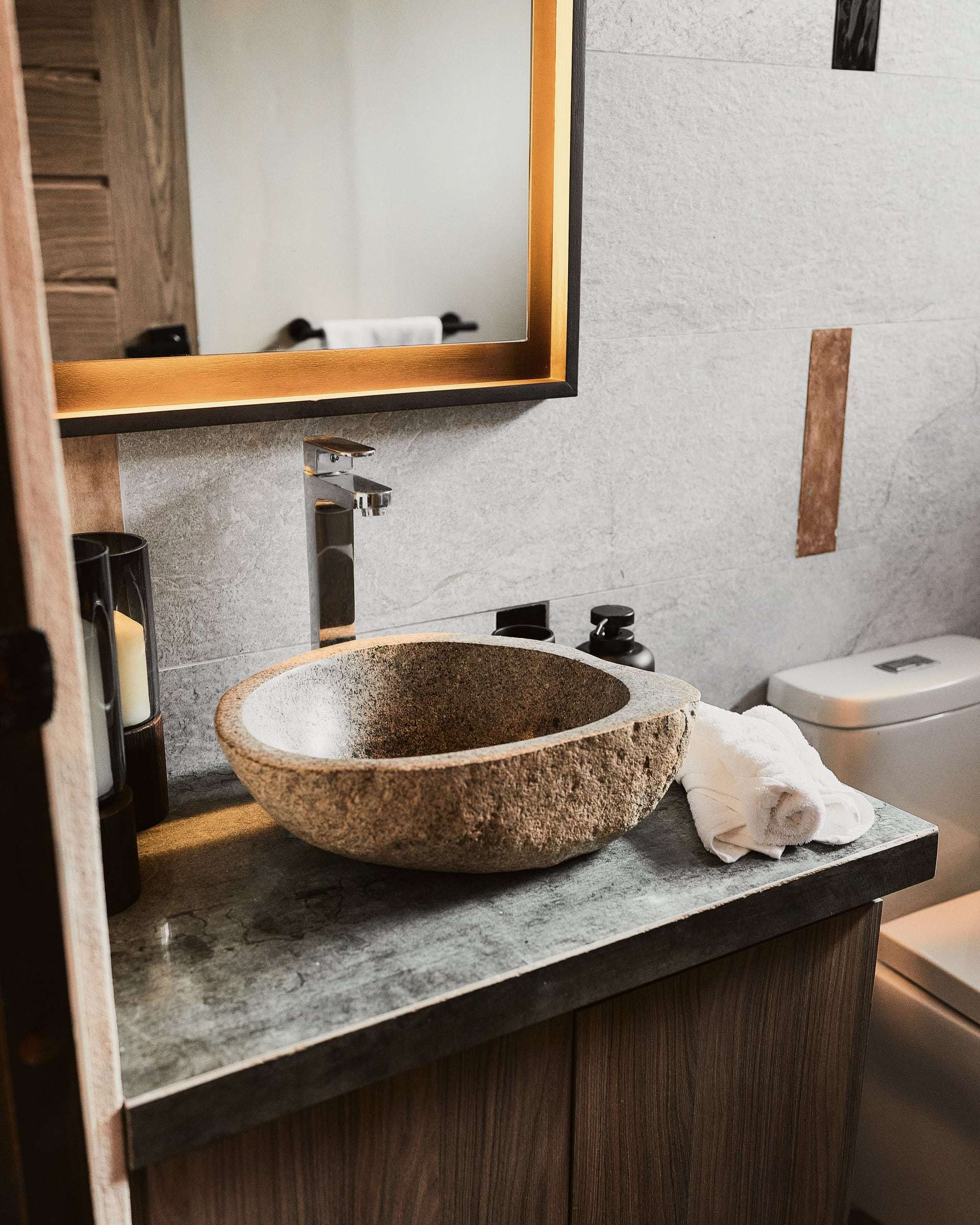 Terrace Suite bathroom: river-stone vessel sink on a grey stone counter, rolled towels and a backlit mirror